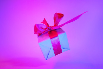 Gift box with red ribbon on trendy neon color background. zero gravity. levitation. copyspace. Concept sales, discount price, christmas presents and shopping