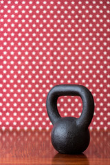 Rustic black kettlebell on a wood floor against a patterned backdrop of red and white