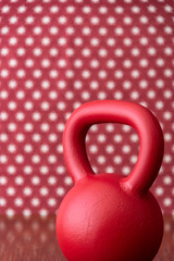 Large red kettlebell on a wood floor against a patterned backdrop of red and white