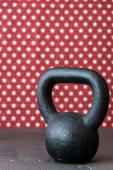 Fototapeta na wymiar Rustic black kettlebell on a black rubber mat floor against a patterned backdrop of red and white