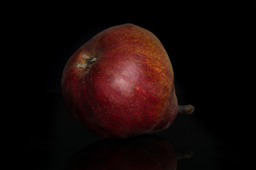 One whole fresh dark red pear anjou isolated on black glass