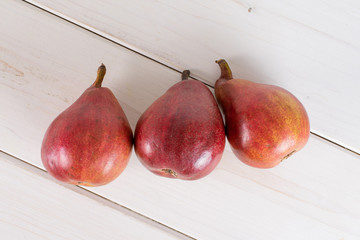 Group of three whole glossy fresh dark red pear anjou flatlay on white wood
