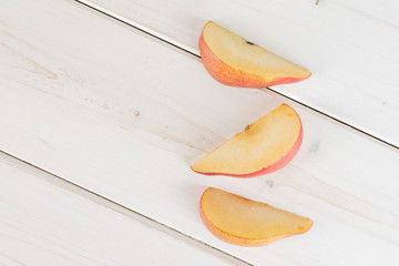 Group of three slices of fresh dark red pear anjou flatlay on white wood