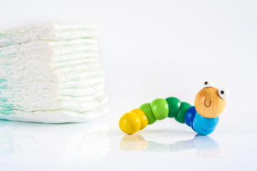 Toy worm with smile next to a pile of diapers, to illustrate concepts of health and childhood intestinal diseases. Isolated on white