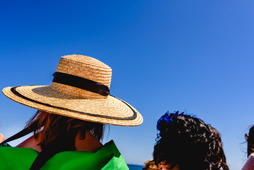 Woman with a wide straw hat to protect herself from the sun, elegantly dressed, during an outdoor event.