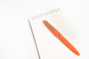 A shiny orange fountain pen together with a spiral-bound notebook.
