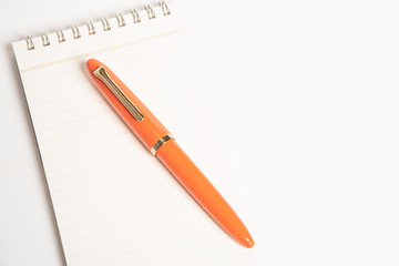 A shiny orange fountain pen together with a spiral-bound notebook.