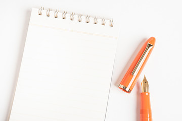 A shiny orange fountain pen together with a spiral-bound notebook.