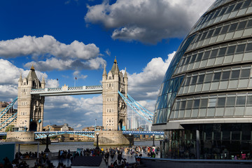 Twin stone towers of Tower Bridge over the Thames River in London with modern curved City Hall...