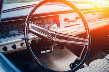 Classic retro or vintage car interior with steering wheel in sunset light, close up