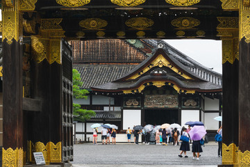 Tourists at the entrance in the Nijo castle in Kyoto in rain with colorful umbrellas during rainy...