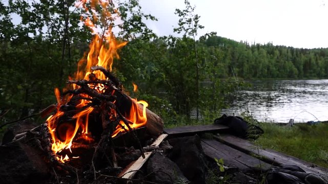 Campfire flames in slow motion with sausage being barbicued on the banks of Torne river in Sweden.