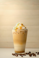 Ice coffee in the glass topped whipping cream with coffee beans. Cold summer drink on wooden background and copy space. Advertising for caramel mocha and chocolate beverage for the cafe.