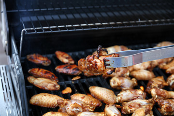 Close up of an open barbecue grill cooking chicken wings with tong holding a single wing