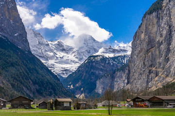 Fototapeta na wymiar Green fields and famous touristic town with high waterfall in background, Lauterbrunnen, Bernese Oberland, Switzerland, Europe