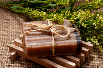 Fresh Aster Solidago Flowers, Wooden Soap Holder and handmade Frankincense & Myrrh Goat's Milk Bar Soap tied with jute rope on burlap background.