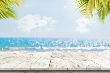 Foto auf Acrylglas Oberseite des Holztisches mit Meerblick und Palmblättern, verschwommenes Bokeh-Licht von ruhigem Meer und Himmel auf tropischem Strandhintergrund. Leer, bereit für Ihre Produktdisplay-Montage. sommerferien hintergrundkonzept. © jakkapan