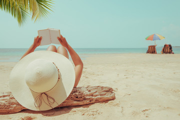 Leisure in summer - Young woman in straw hat lying sunbathe on a tropical beach, relax with book. Memories of summer vacation concept. retro color tone.