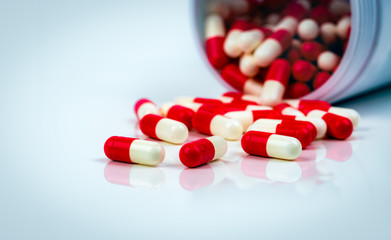 Red-white capsule pills on white table on blurred background of drug bottle. Antibiotics drug resistance. Antimicrobial capsule pills. Pharmaceutical industry. Pharmacy. Global healthcare concept.