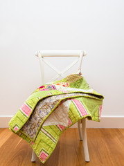 Finished handmade green and pink patchwork quilt draped on a white chair with copy space