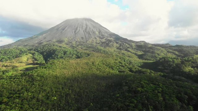Aerial pan view of Arenal Volcano, Costa Rica, with clouds and sunlight