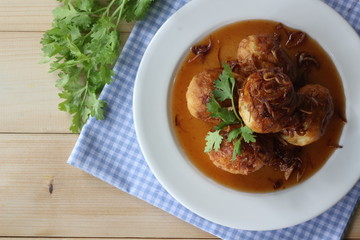 Sweet and sour eggs in white dish with coriander on wooden table.