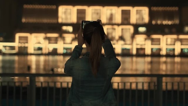 Rear view of a charming tourist girl taking photo or video of fountains