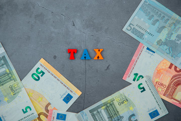 The multicolored tax word is made of wooden letters on a grey plastered wall background.