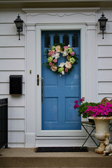 Close up view of a blue door decorated with an attractive wreath of flowers on a white house