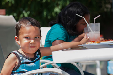 A latino boy and girl enjoying their pizza and limonade lunch meal during the summertime.