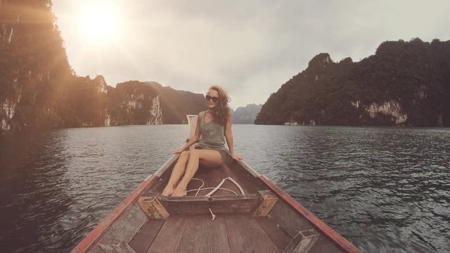Lifestyle video of pretty travel woman sitting in wood long tail boat on tropical limestone cliffs . Explore and vacation concept. Khao Sok lake, Thailand.