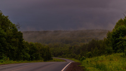 Wet asphalt after rain. Thick rain clouds. The road along the forest. Ural Mountains in rainy summer weather