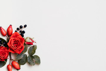 Autumn floral arrangement. Red and black fall berries, green leaves and roses on white background....