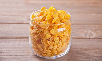 A bowl of dry corn flakes cereal on wooden background
