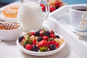 Fresh sweet berries on the white plate, bagel, cup of coffee and honey for breakfast.
