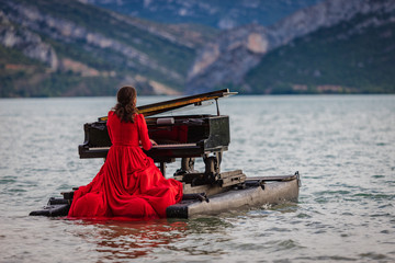 woman dressed in red playing the piano on a lake © Fernando