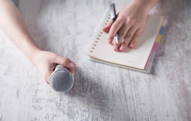 Hand holding microphone and writing on notepad.
