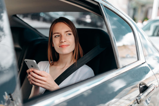 Young woman holding a smartphone  sitting in the car look out in the window- Image