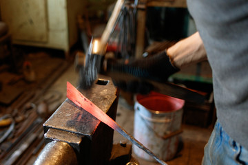 Blacksmith forging red-hot metal with hammer.