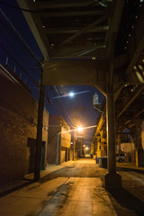 Fototapeta na wymiar Dark and eerie Chicago urban city alley night scenery with vintage elevated CTA train tracks