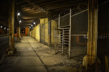 Old fence gate entrance with barbwire under a vintage urban city bridge in Chicago at night