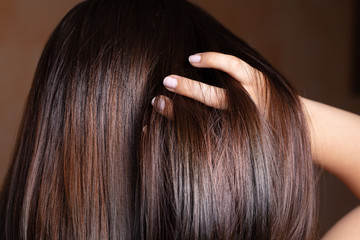 A closeup view of a beautiful young Caucasian woman stroking her fingers through her long brunette straightened hair. Hairstyling before an event.