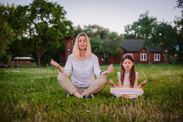 Mother and daughter child meditate together in Lotus position outdoors.