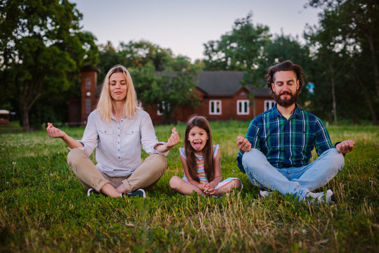 Mother father and daughter child meditate together in Lotus position outdoors.