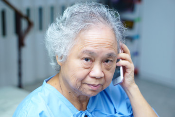 Asian senior or elderly old lady woman patient with credit card talking on the mobile phone while sitting and happy on bed in nursing hospital ward : healthy strong medical concept 