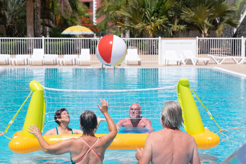 Group of senior people playing in swimming pool with floating volleyball net and ball. Happiness in...