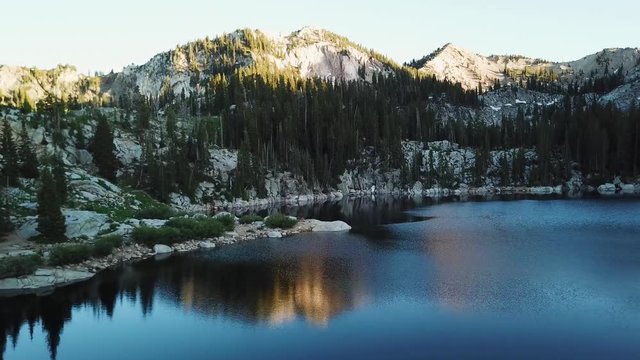 Drone Shot smoothly gliding over a lake high up in the Utah Mountains. The reflection of the mountains can be seen on the lake as the drone flies across.