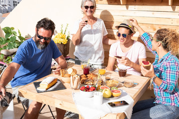 Four people smiling together and one dog. Caucasian family with parents, teenager son and grandmother. Wooden table with homemade cakes, fruit and coffee.