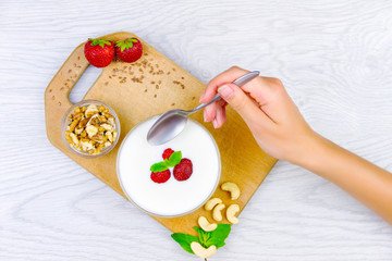 Healthy fitness low calories breakfast: yogurt with cashew and walnuts for healthy lifestyle and fitness diet isolated on white background. Hands with spoon ready for breakfast. Healthy food concept