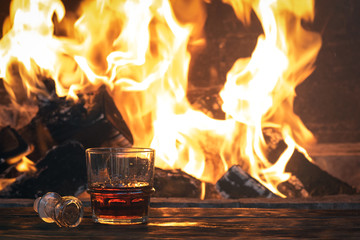 Strong alcohol in a transparent glass on a wooden table on a burning fire background.